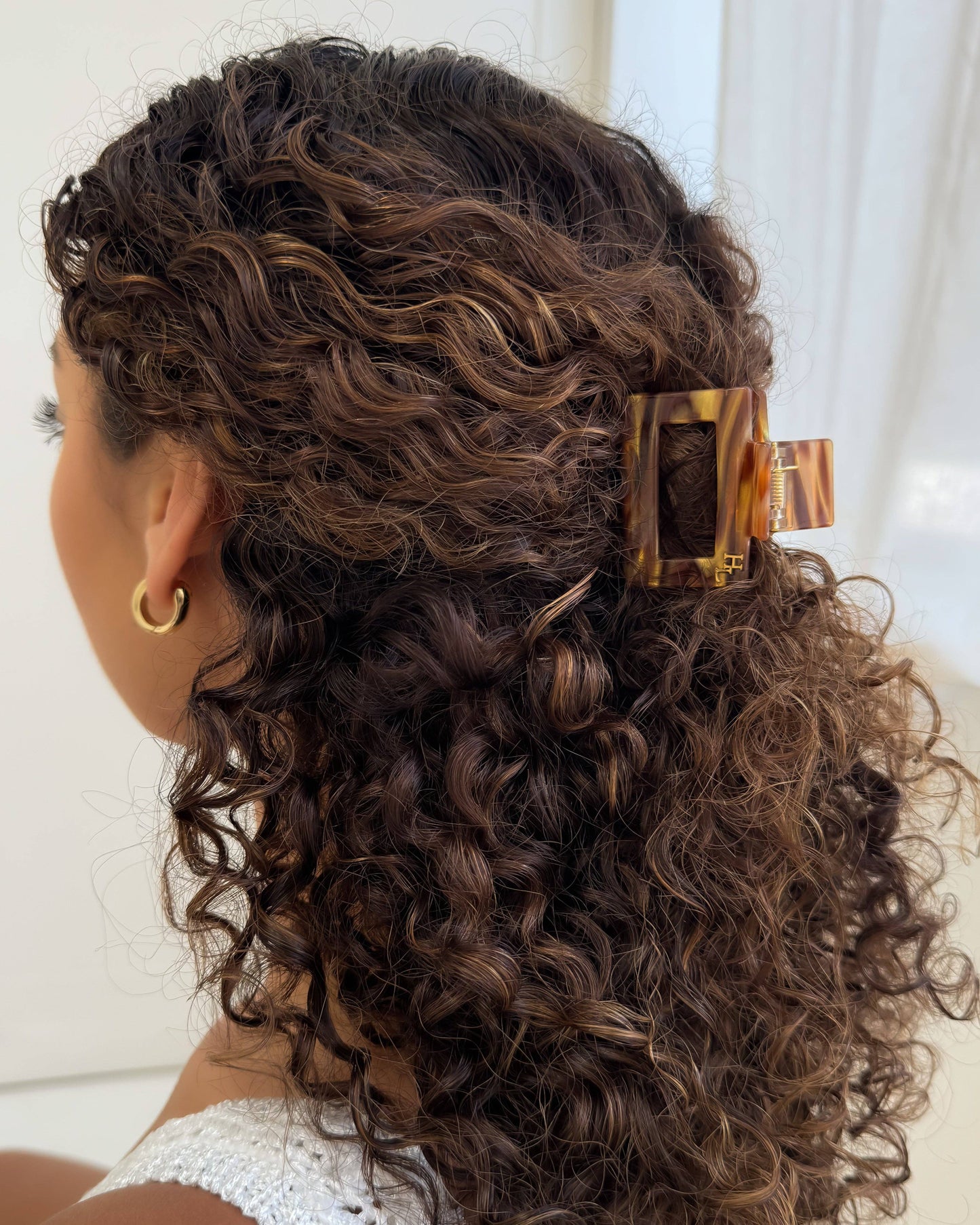 Woman with curly hair wearing the HoneyLux Ecofriendly Acetate Midi Clip in the color Hazel Honey against a neutral background