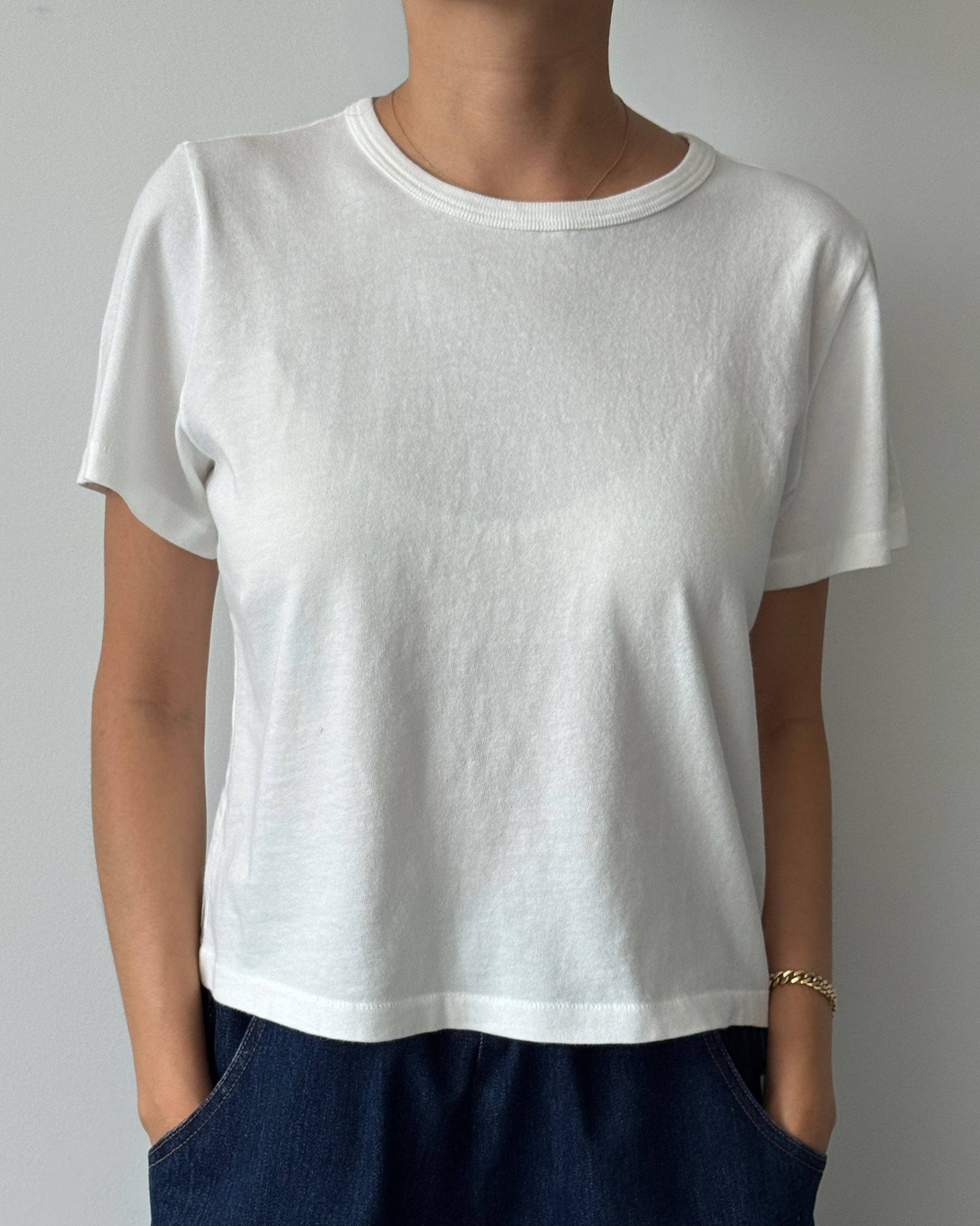 Person wearing a plain white t-shirt and dark pants against a neutral background