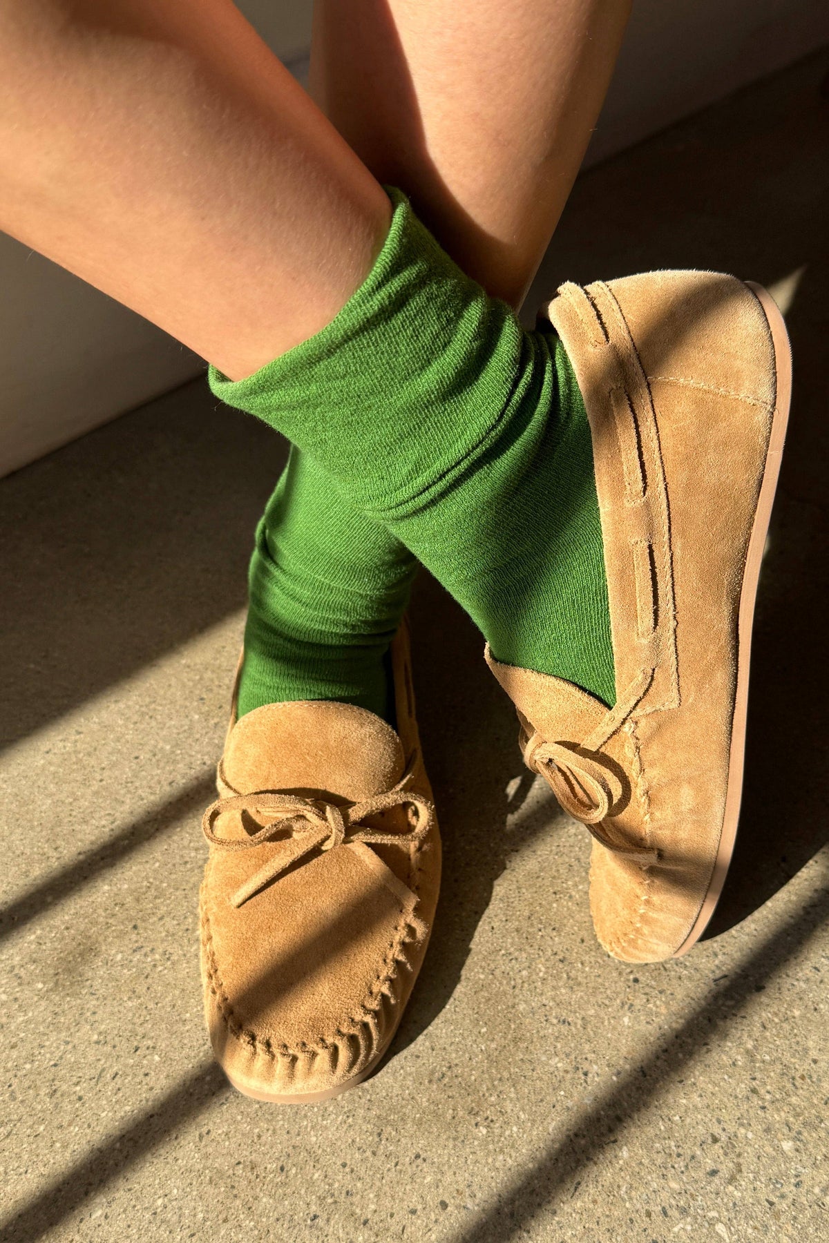 Person wearing green socks and tan moccasins on a concrete floor.