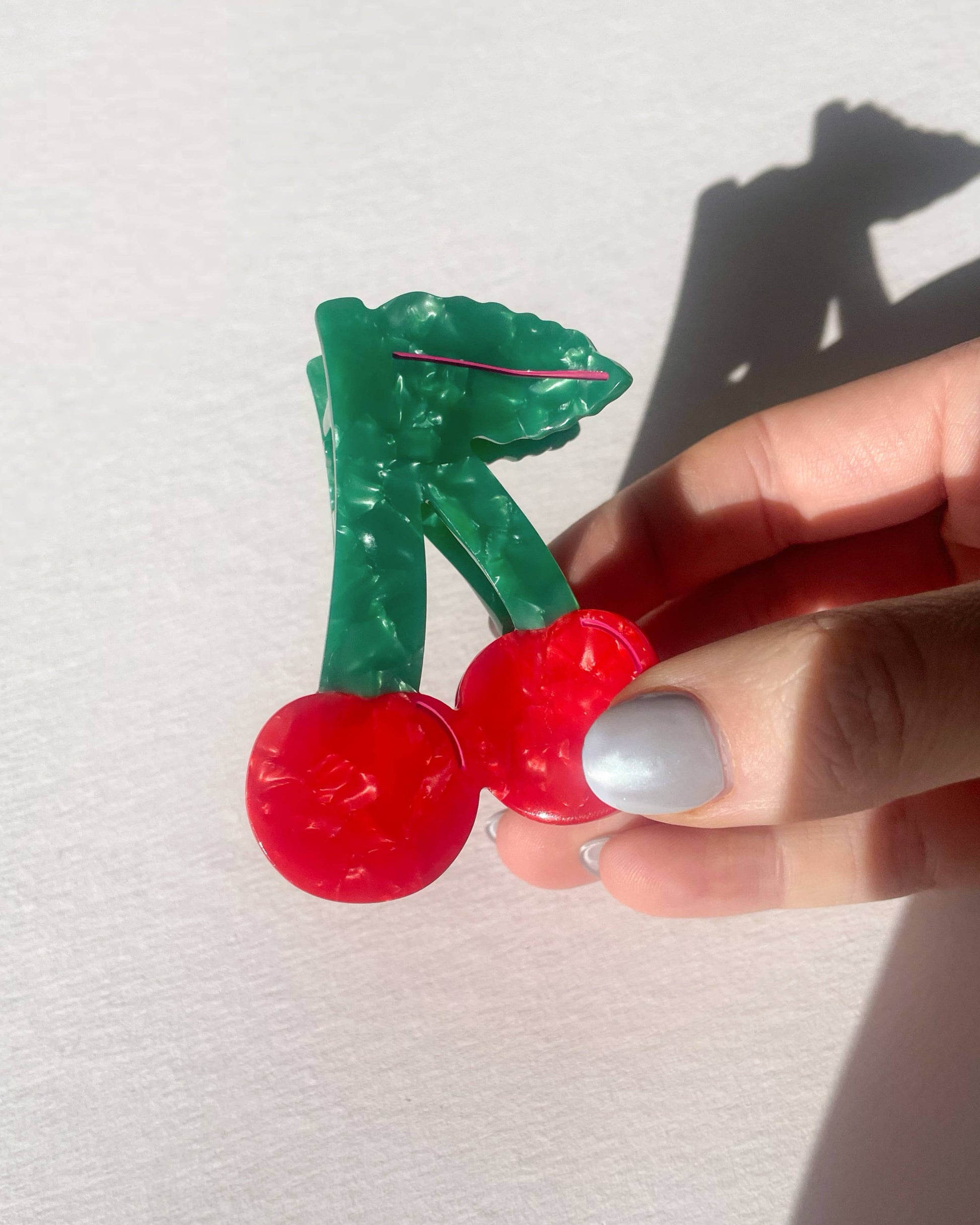 Hand holding a cherry shaped hair clip against a white background