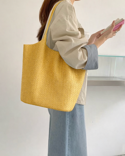 Person holding a yellow woven tote bag in an indoor setting