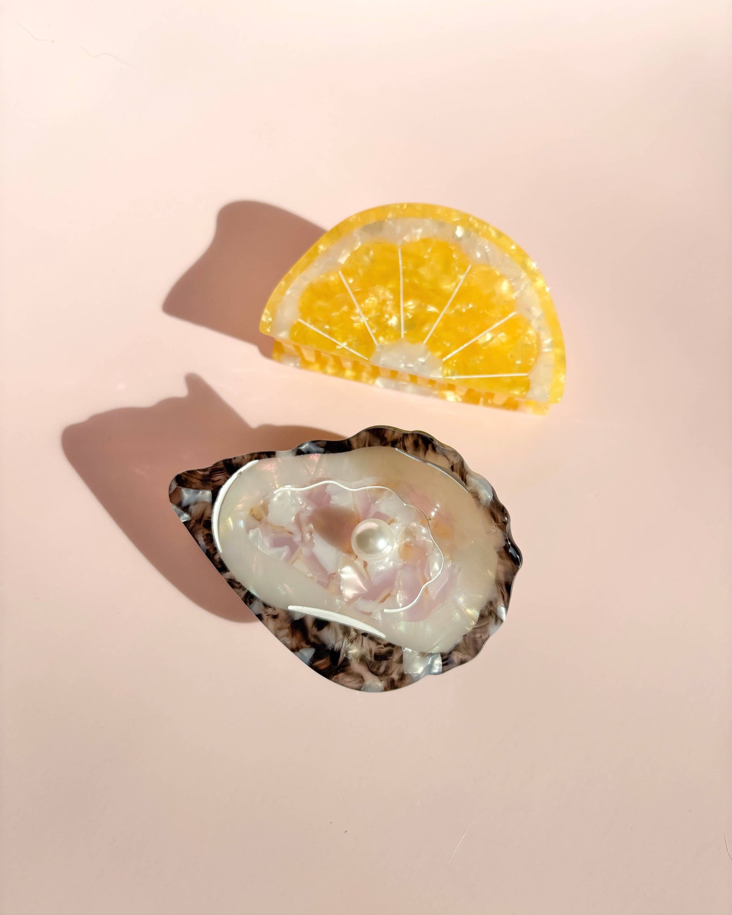 Front view of the Line&Co oyster and lemon claw clip laying on a pink background