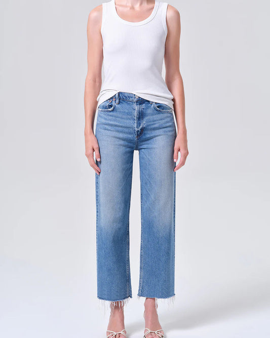 Person wearing a white tank top and light blue jeans on a plain background