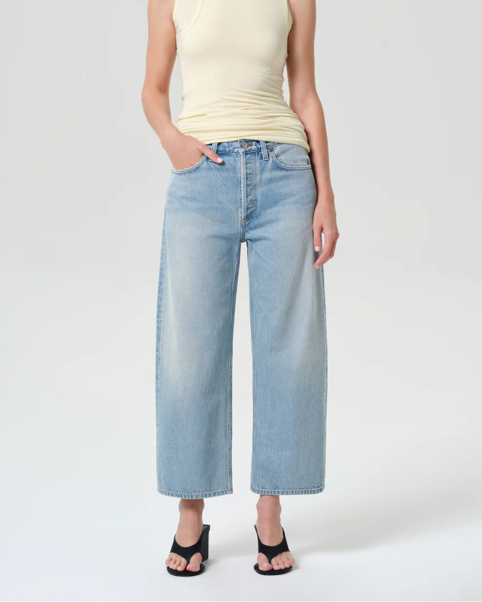 Person wearing a light-colored sleeveless top and light blue jeans on a white background