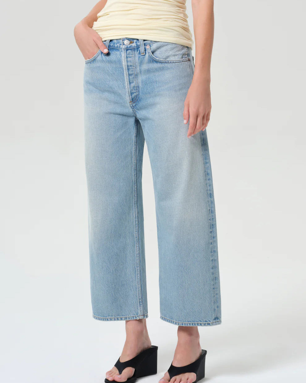 Person wearing light blue jeans and a yellow top on a white background