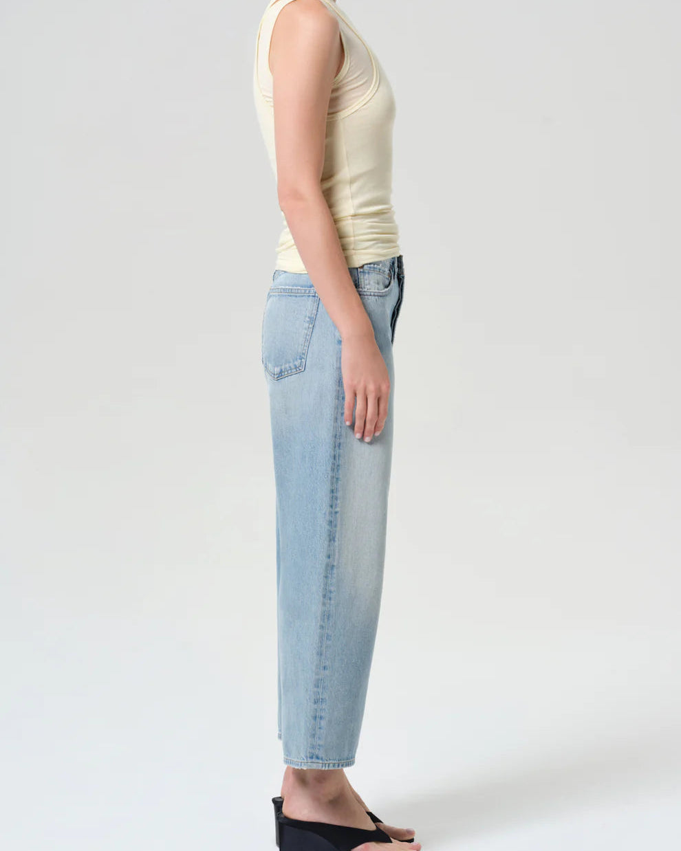 Person wearing a light-colored sleeveless top and light blue jeans on a white background
