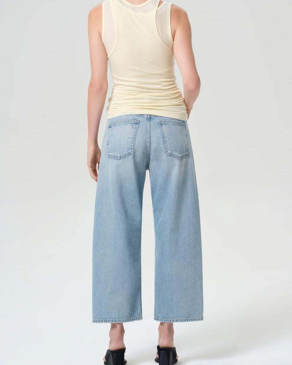 Person wearing a cream sleeveless top and light blue jeans on a white background
