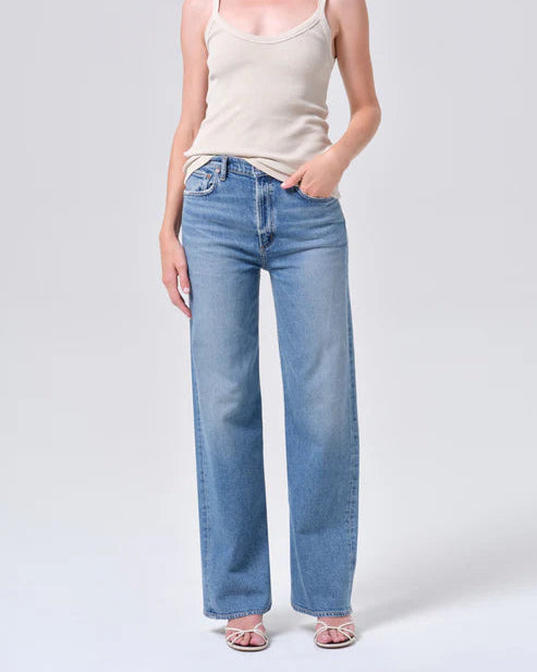 Person wearing a beige tank top and light blue jeans on a white background