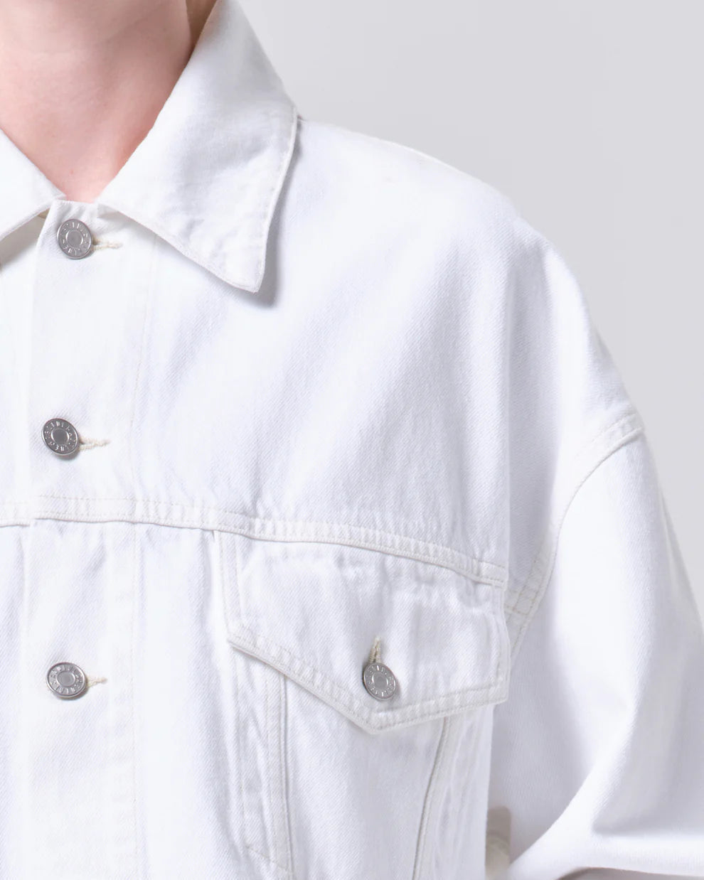 Close-up of a white denim jacket with button details on a plain background