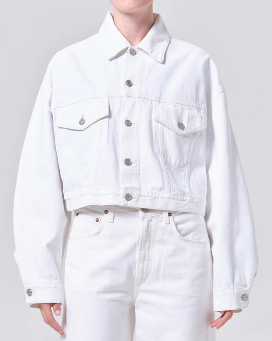 Person wearing a white denim jacket and pants on a plain background