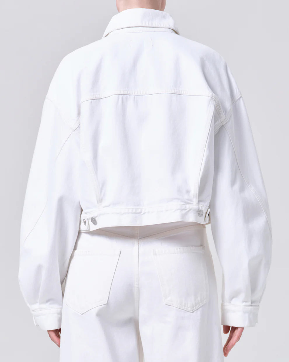 Person wearing a white denim jacket and pants on a plain background