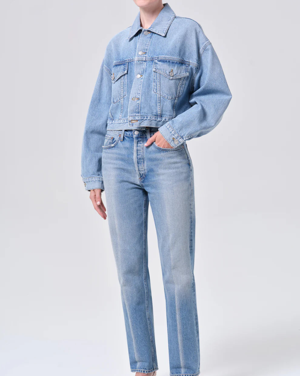 Person wearing a light blue denim jacket and jeans on a white background