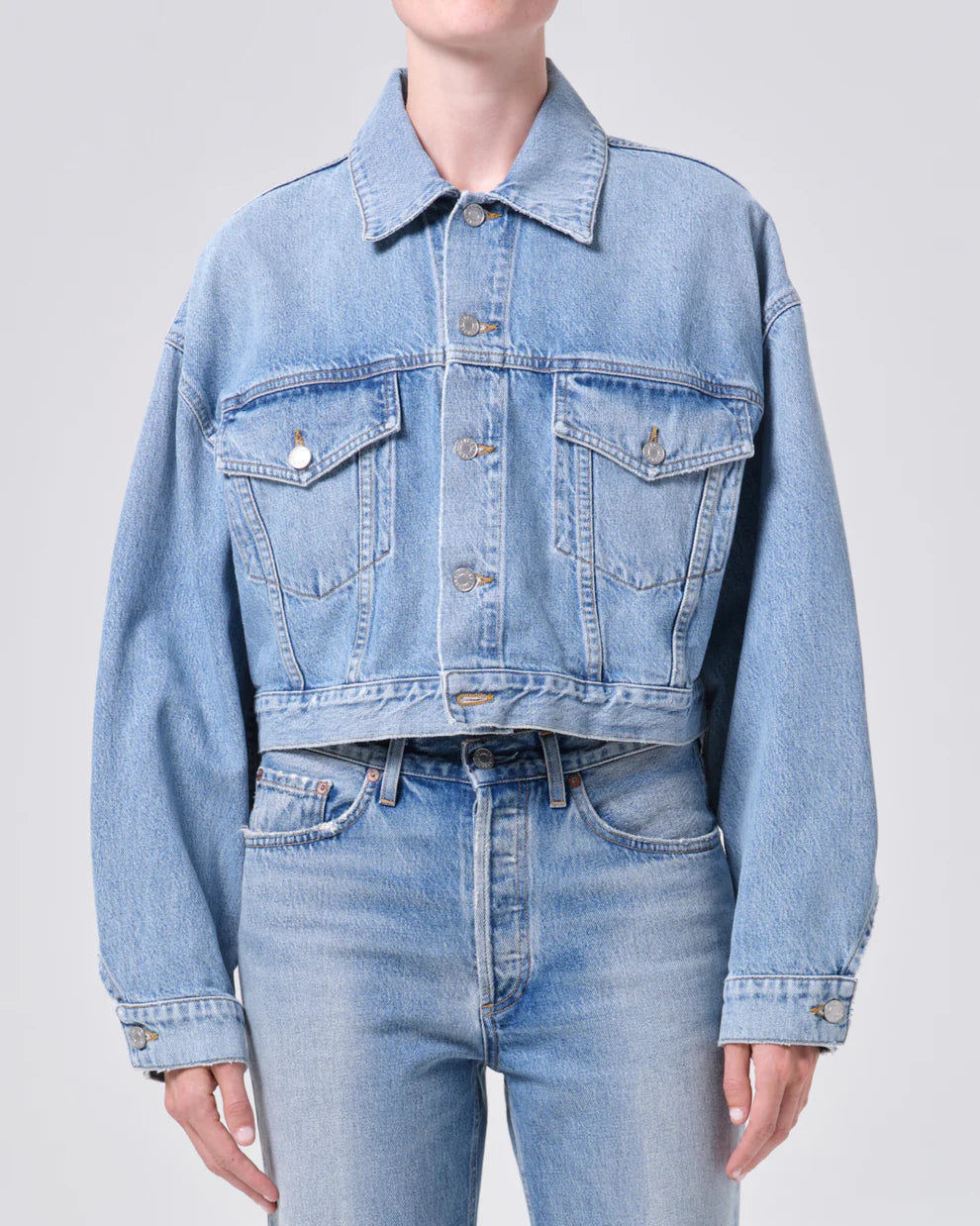 Person wearing a light blue denim jacket and jeans on a plain background