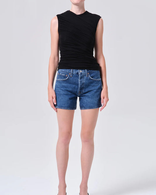 Person wearing a black sleeveless top and blue denim shorts on a white background