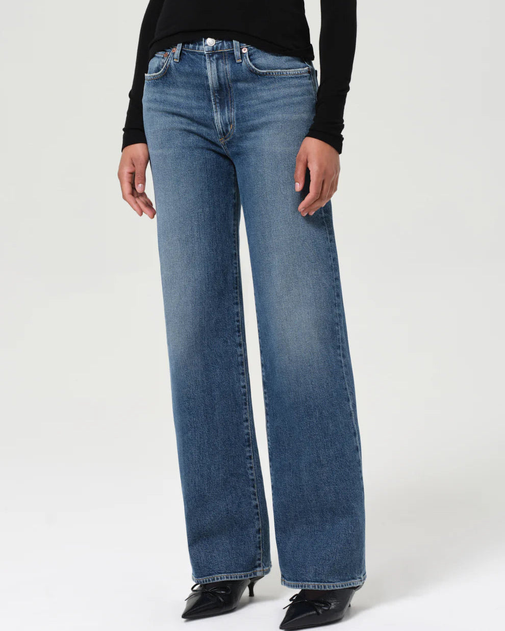 Person wearing blue jeans and a black top on a white background