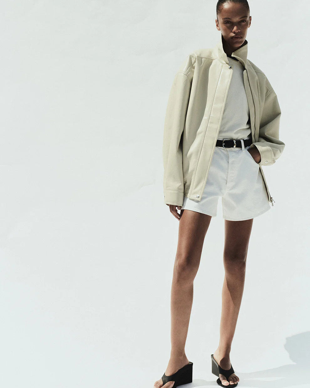 Person wearing a beige coat, white shirt, and shorts on a white background