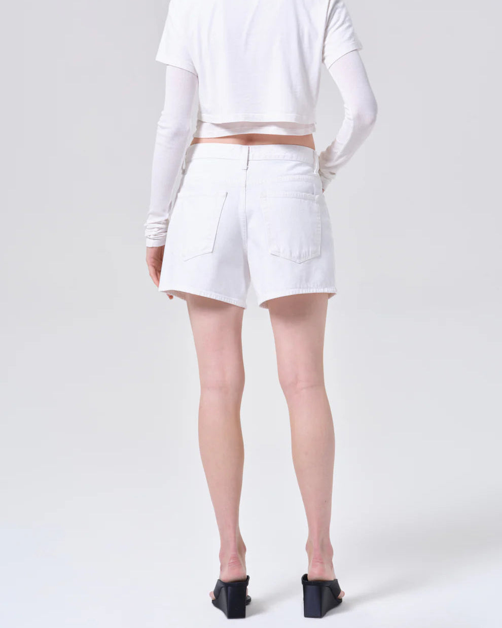 Person wearing a white long-sleeve crop top and white shorts on a light gray background