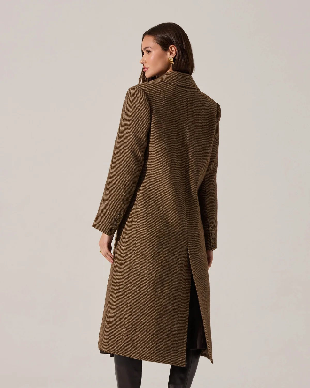 Woman wearing a long brown coat on a plain background