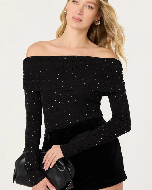 Woman wearing a black off-shoulder top with long sleeves and a matching skirt on a white background.