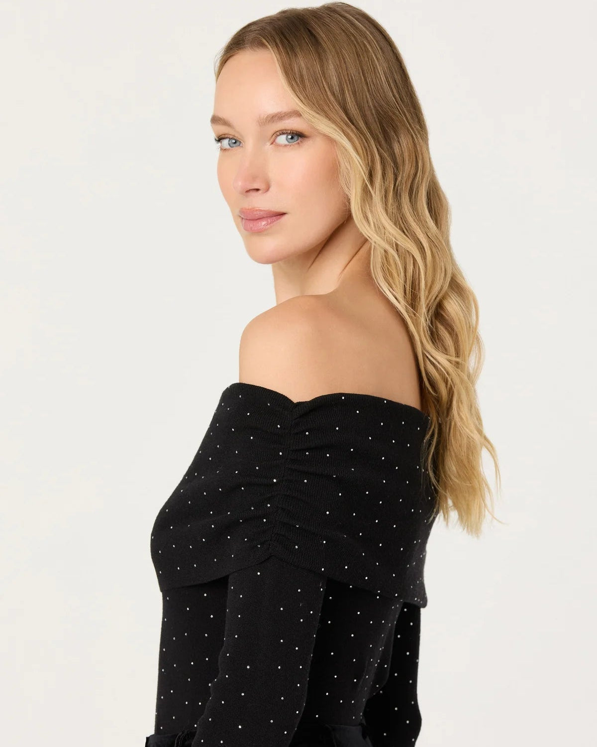 Woman wearing a black off-shoulder top with white polka dots on a white background