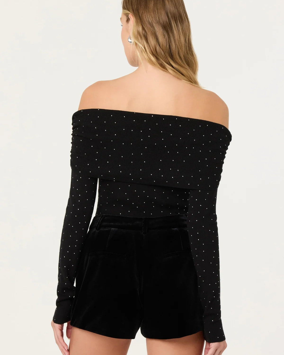 Woman wearing a black off-shoulder top with long sleeves and black shorts on a white background