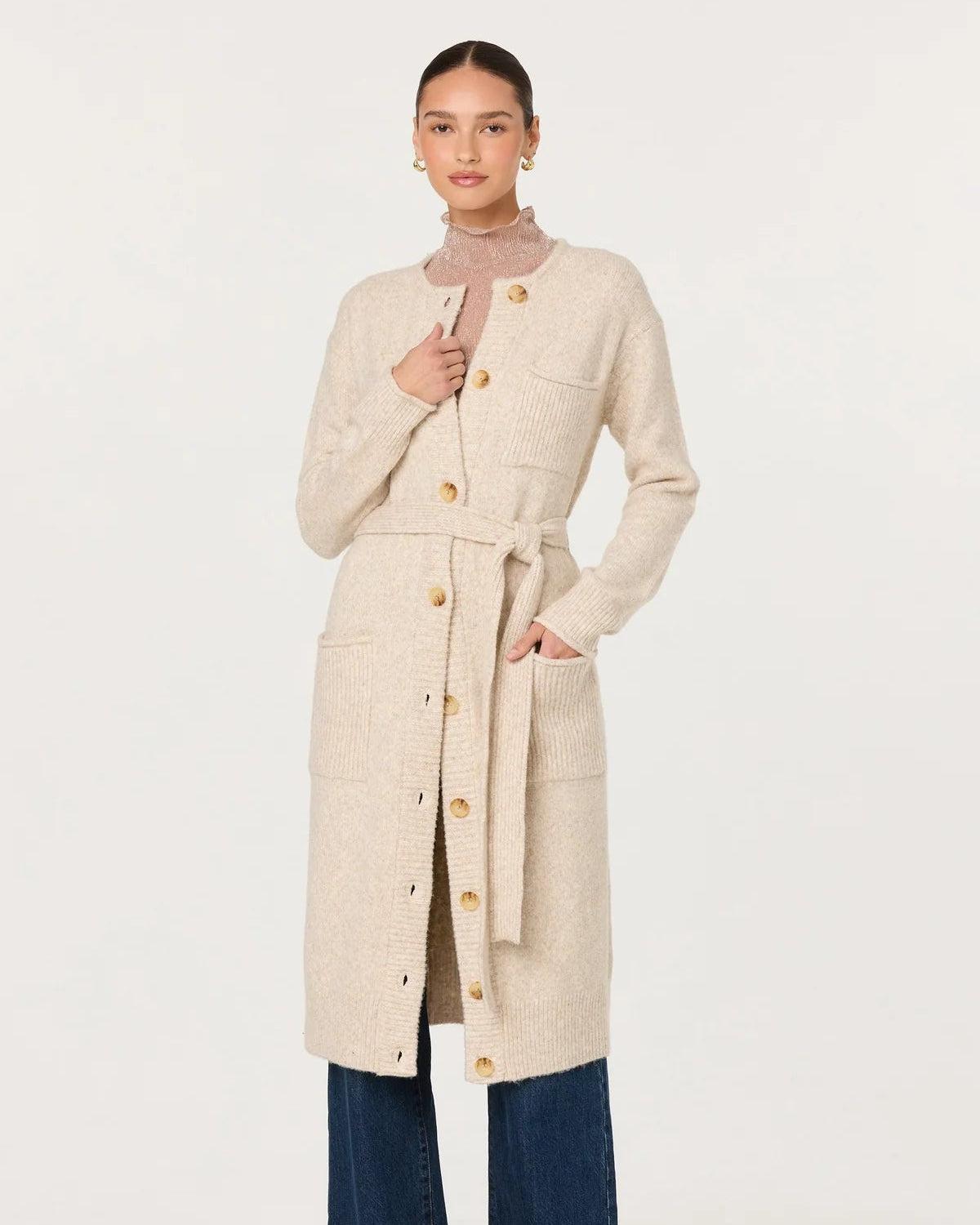 Woman wearing a long beige coat with a belt, standing against a white background