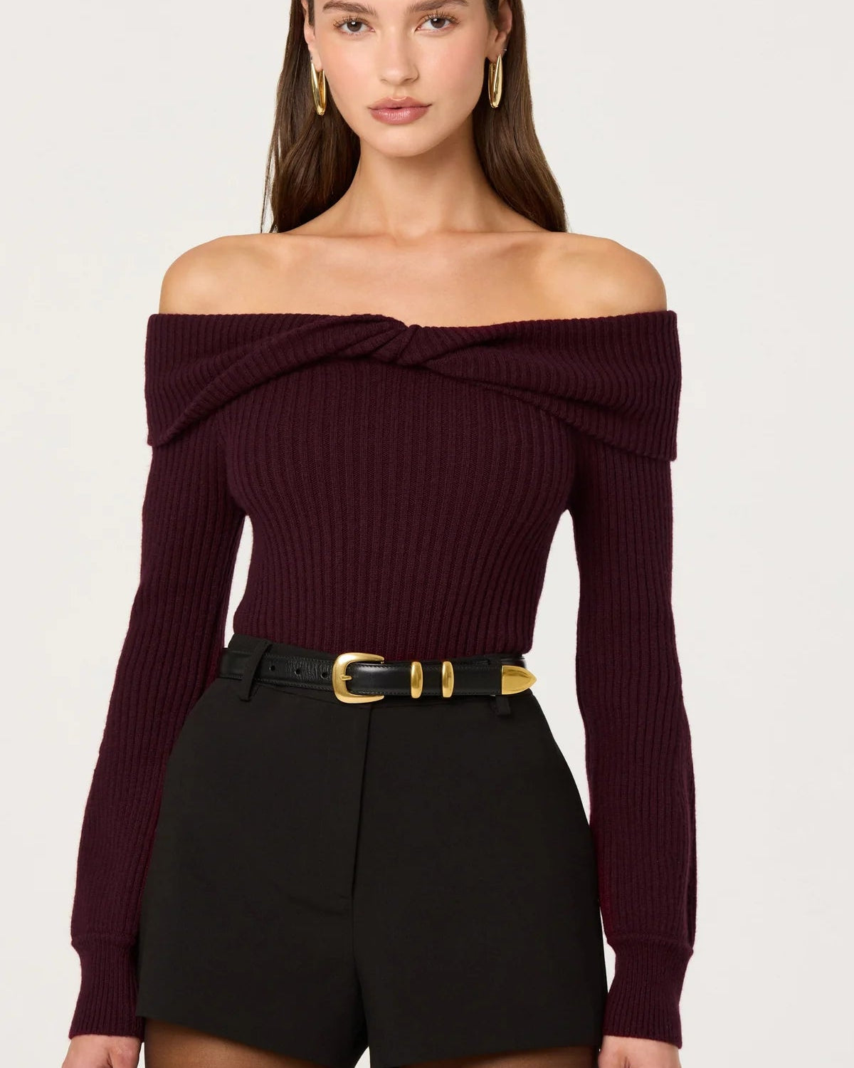 Woman wearing a burgundy off-shoulder top with a black belt and shorts on a white background