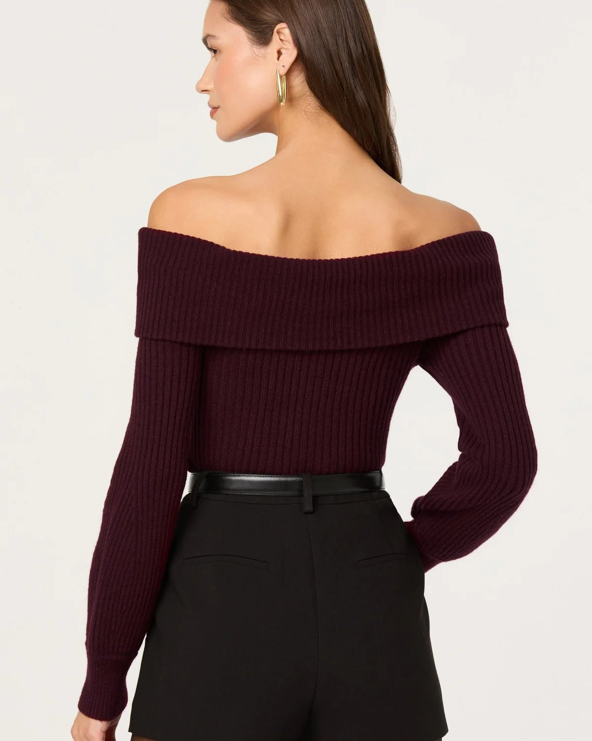 Woman wearing a burgundy off-shoulder sweater and black shorts on a white background