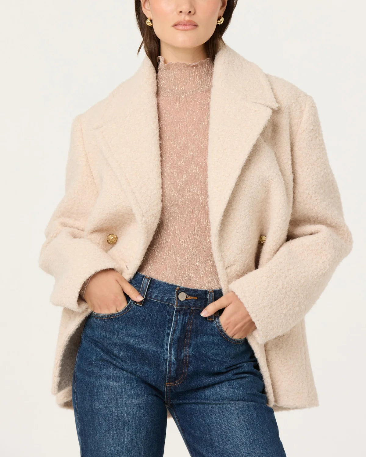 Woman wearing a beige coat, brown sweater, and blue jeans on a white background