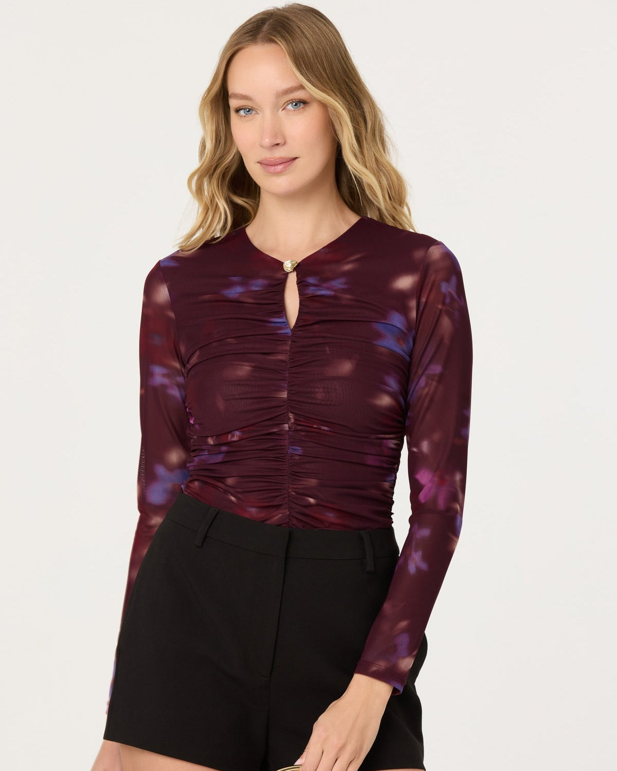 Woman wearing a burgundy floral top and black shorts on a white background