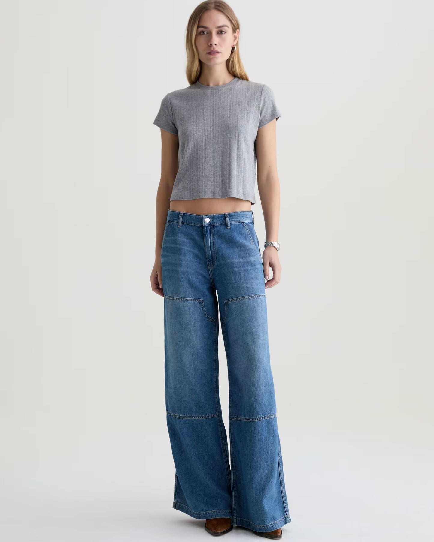 Woman wearing a gray crop top and blue wide-leg jeans on a white background