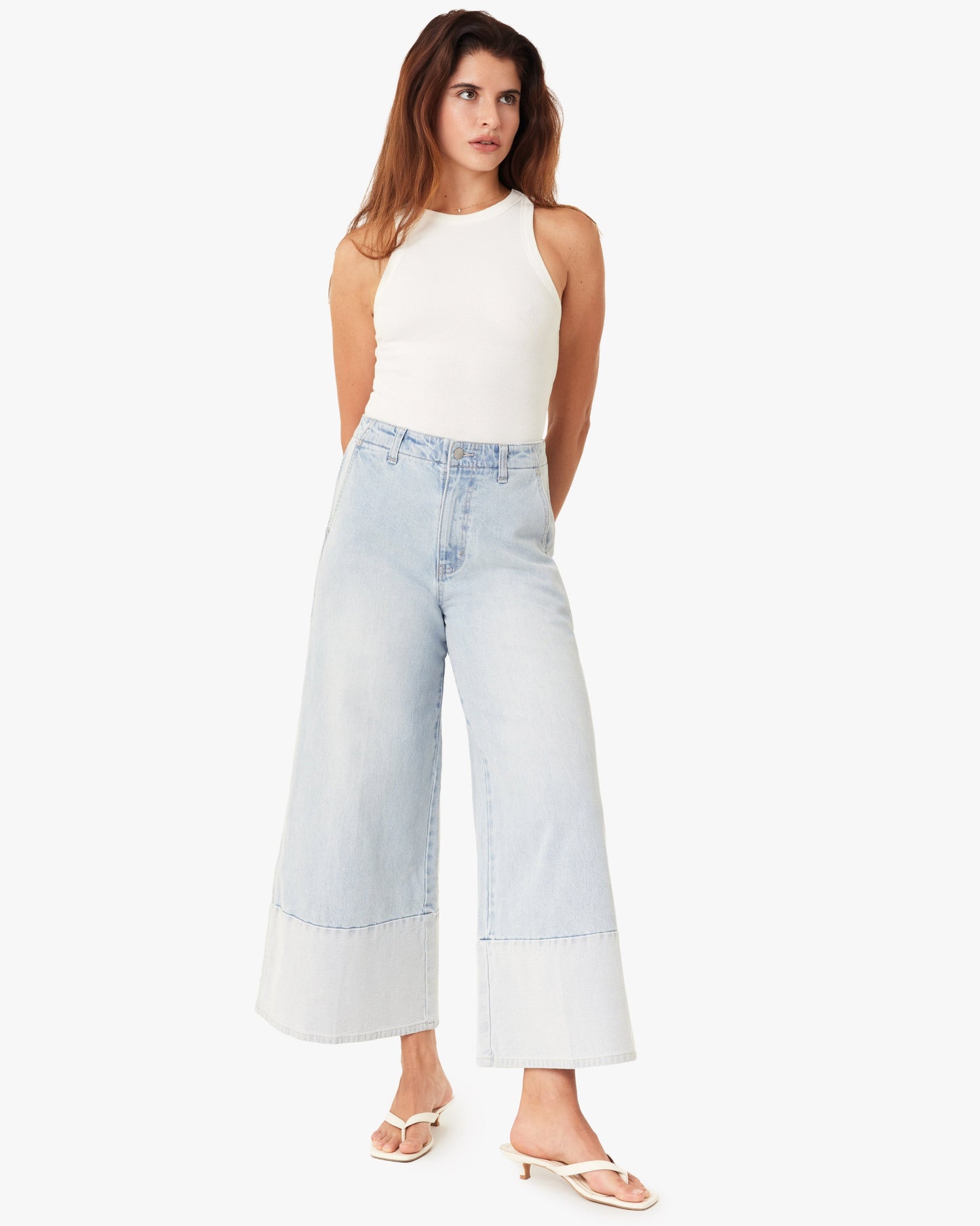 Woman wearing a white sleeveless top and light blue wide-leg jeans on a white background