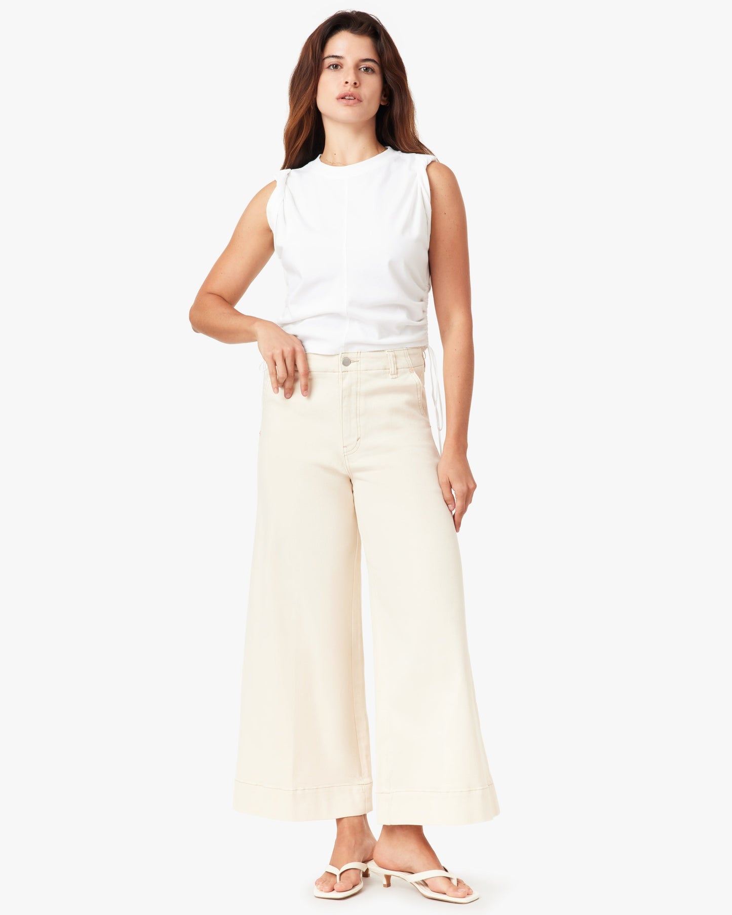 Woman wearing a white sleeveless top and light-colored pants on a white background
