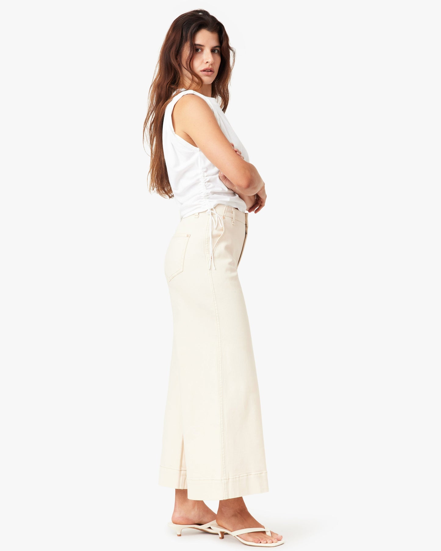 Woman wearing a white sleeveless top and beige pants on a white background