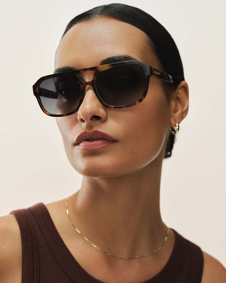 Woman wearing dark sunglasses and a brown top against a plain background