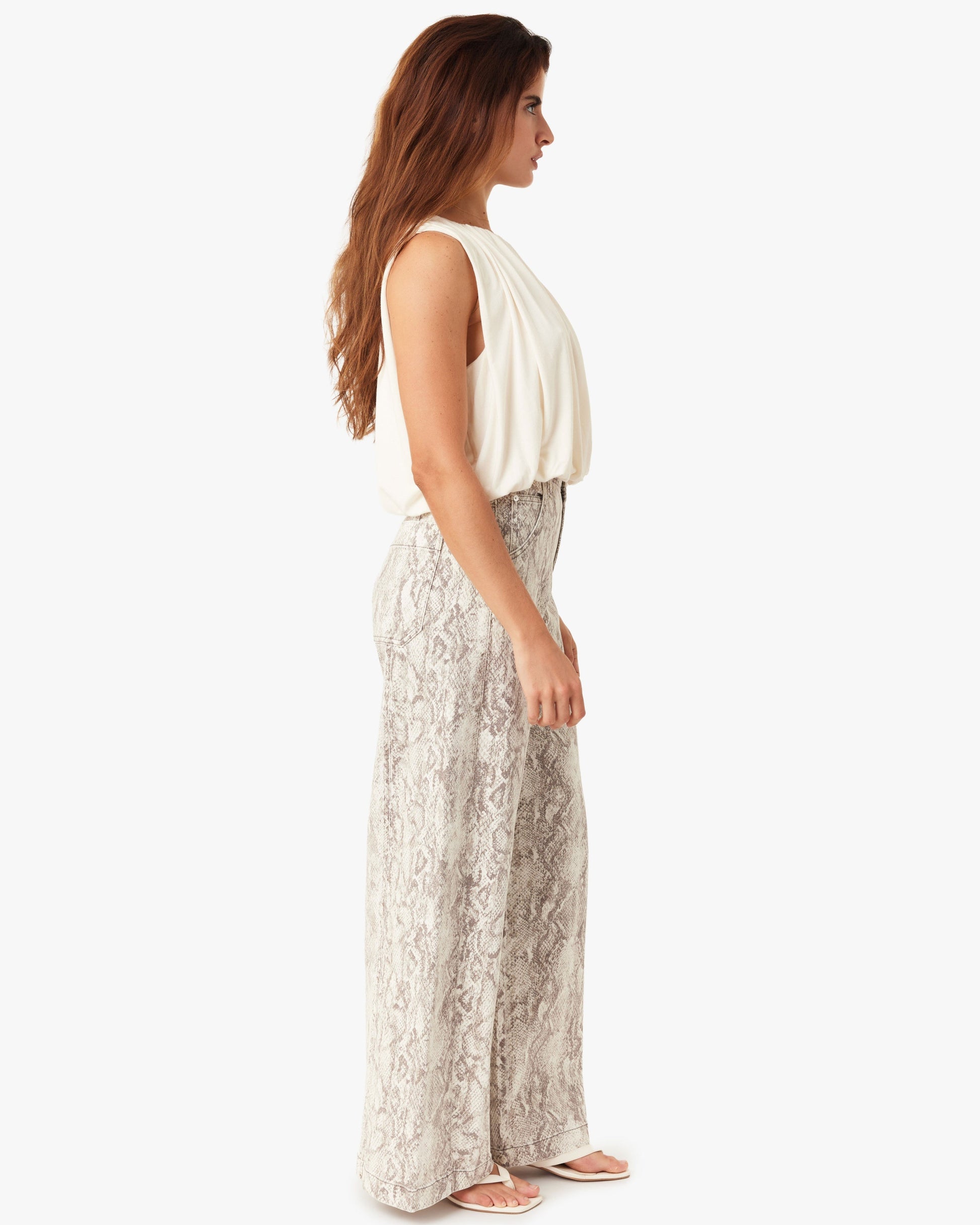 Woman wearing a white sleeveless top and light-colored floral pants on a white background