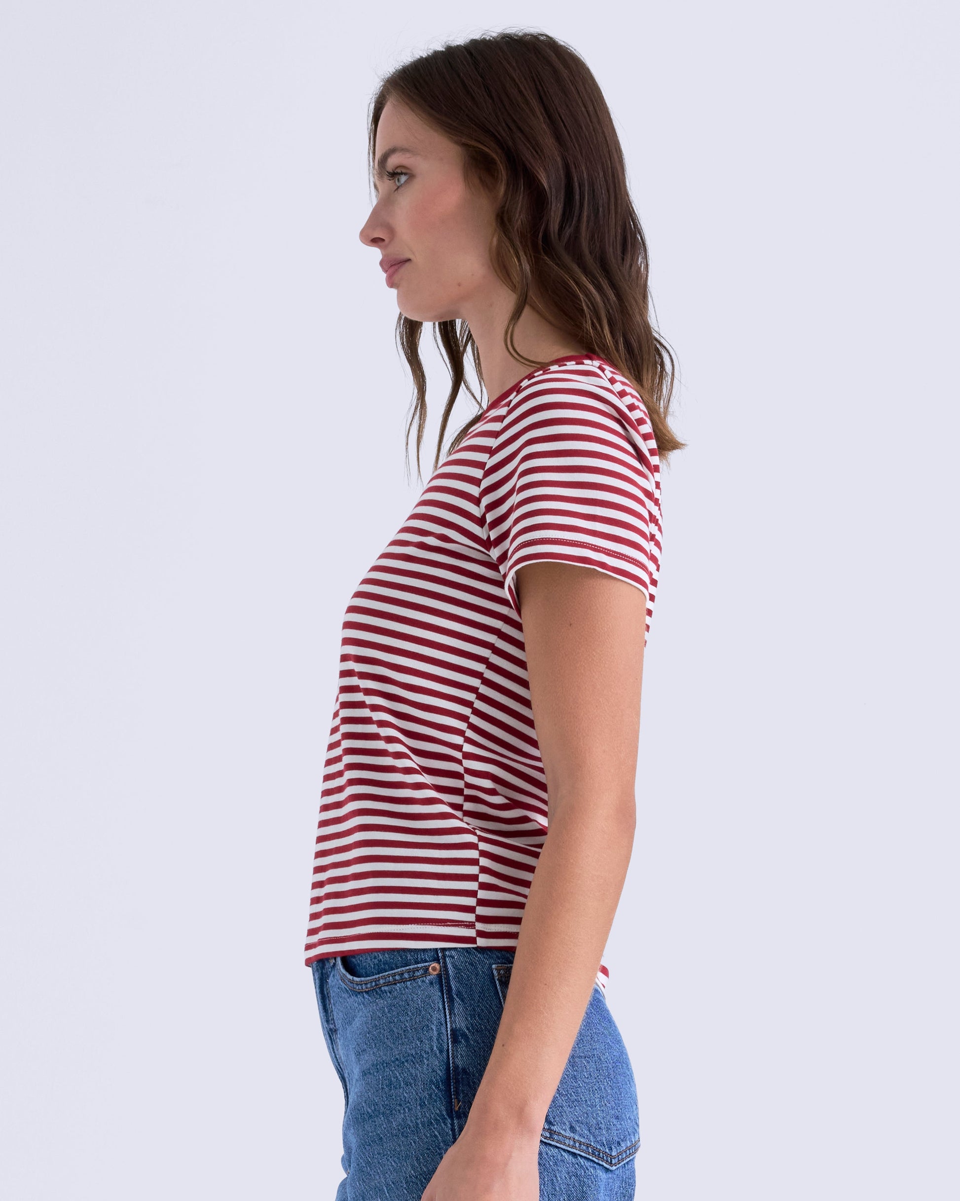 Woman wearing a red and white striped shirt and blue jeans on a light gray background