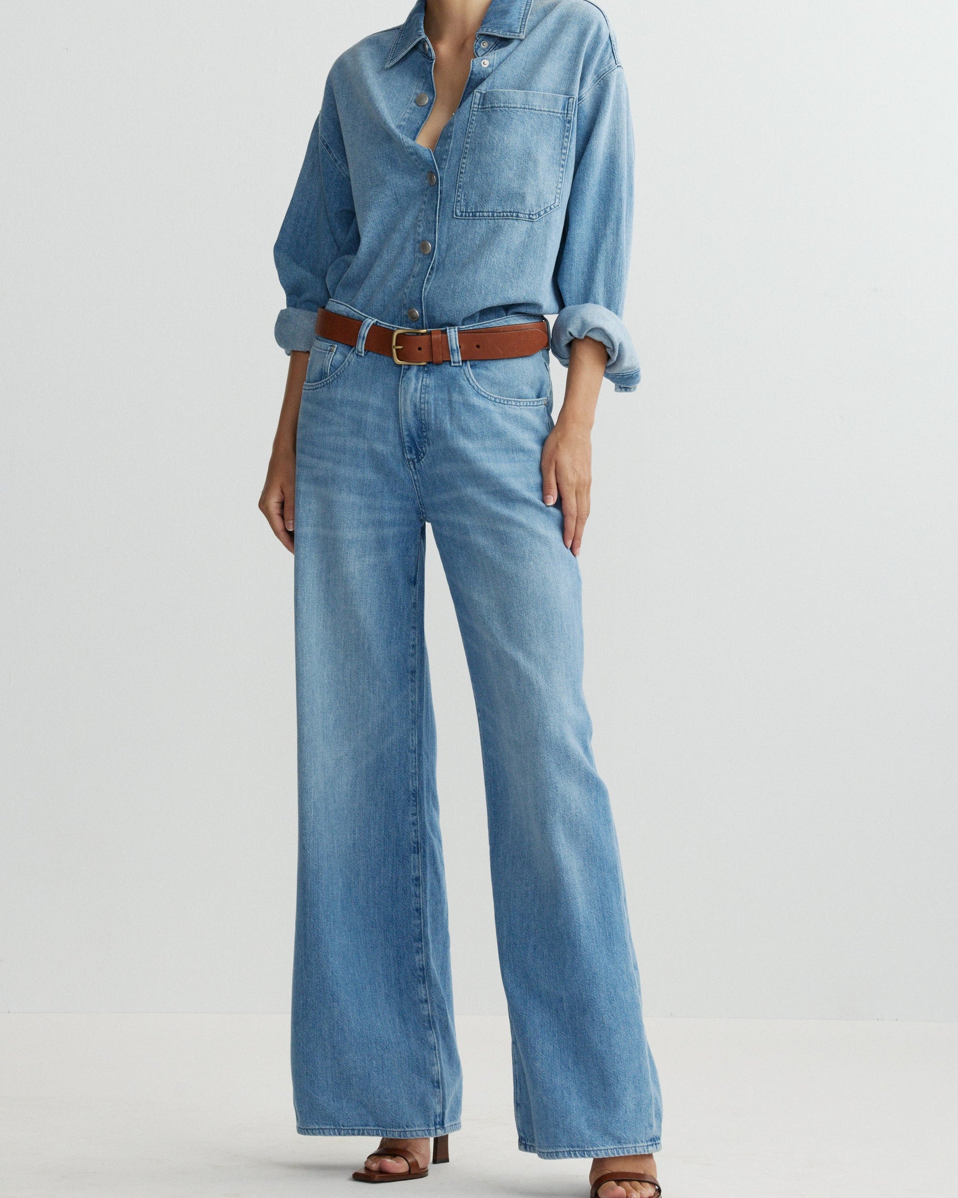 Person wearing a denim shirt and wide-leg jeans on a light gray background