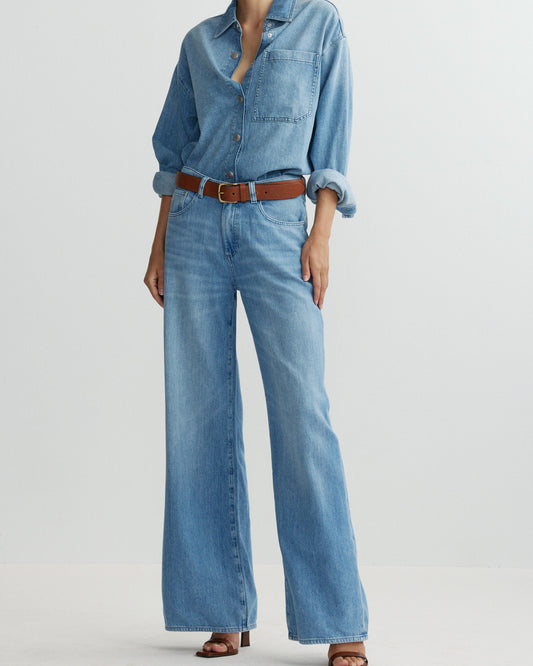 Person wearing a denim shirt and wide-leg jeans on a light gray background