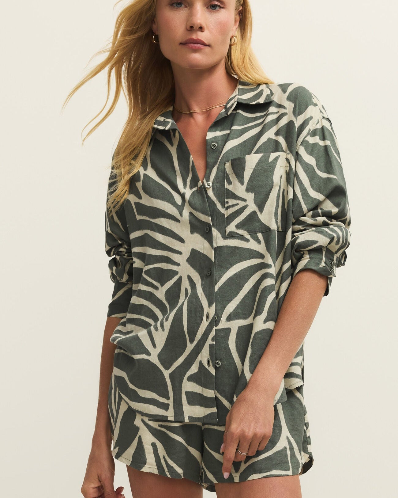 Woman wearing a green and white patterned shirt and shorts set on a beige background