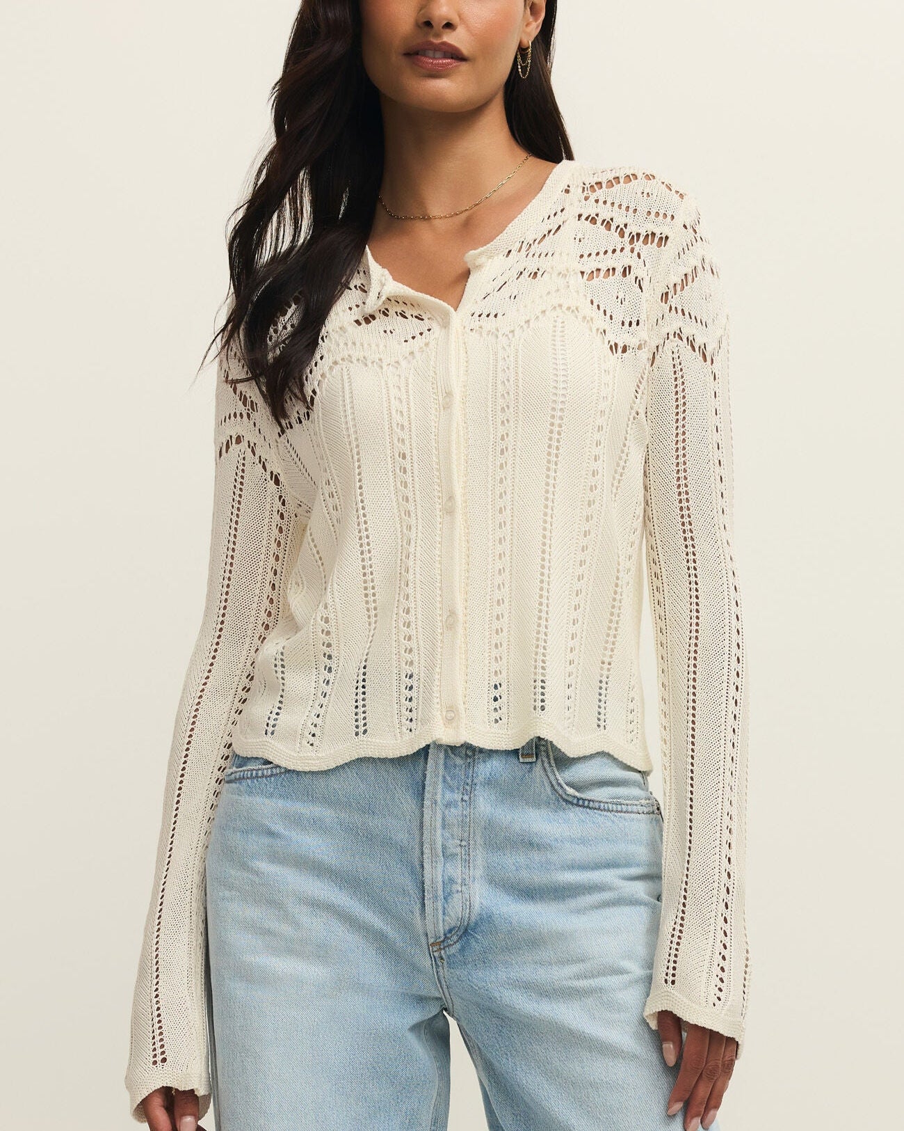 Woman wearing a white lace blouse and light blue jeans against a beige background