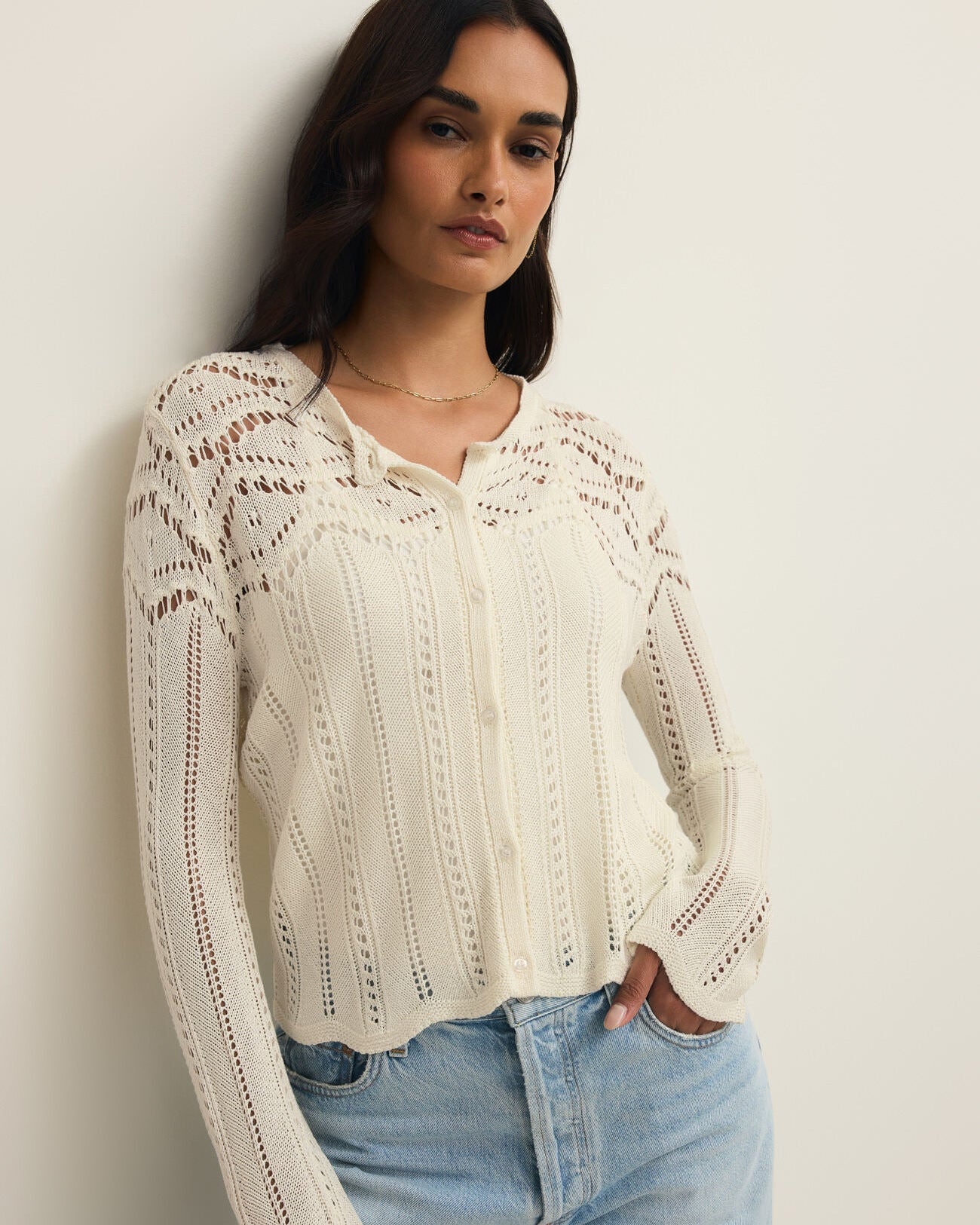 Woman wearing a white lace blouse and light blue jeans against a plain background