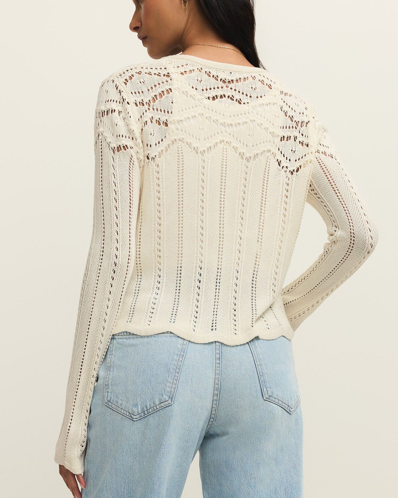 Woman wearing a beige crochet cardigan and light blue jeans on a plain background