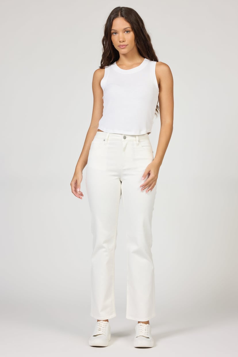 Woman wearing a white sleeveless top and white pants on a plain background