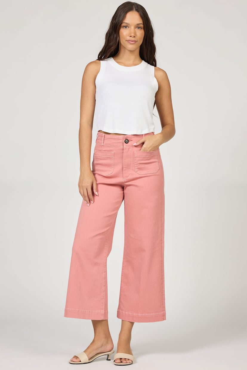 Woman wearing a white sleeveless top and pink pants on a plain background