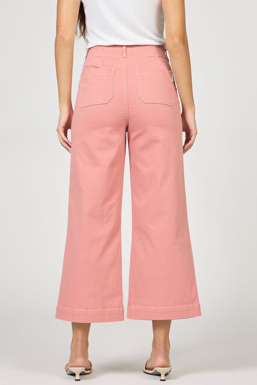 Person wearing pink wide-leg pants and a white top on a plain background