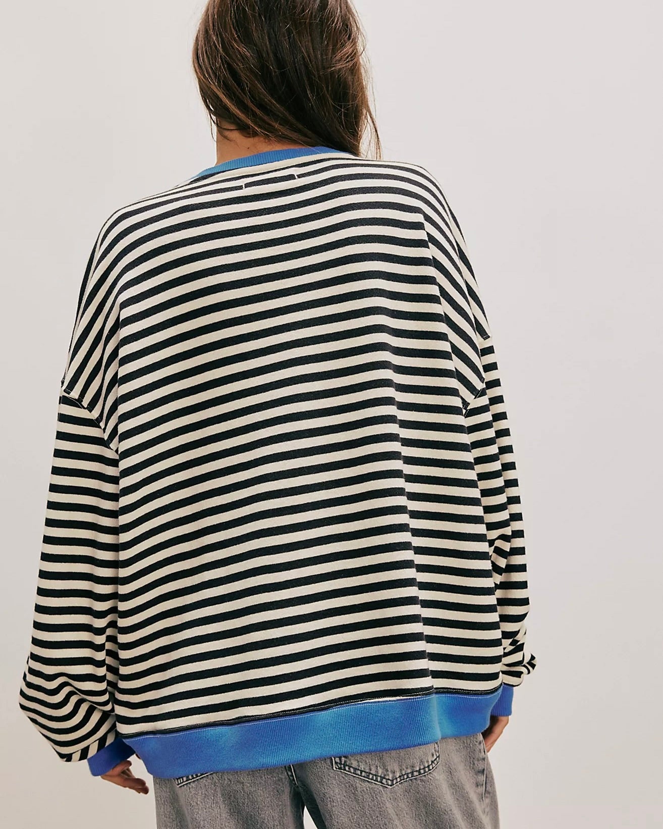 Back view of model standing wearing the Free People Classic Striped Oversized Crewneck in front of a white wall. 