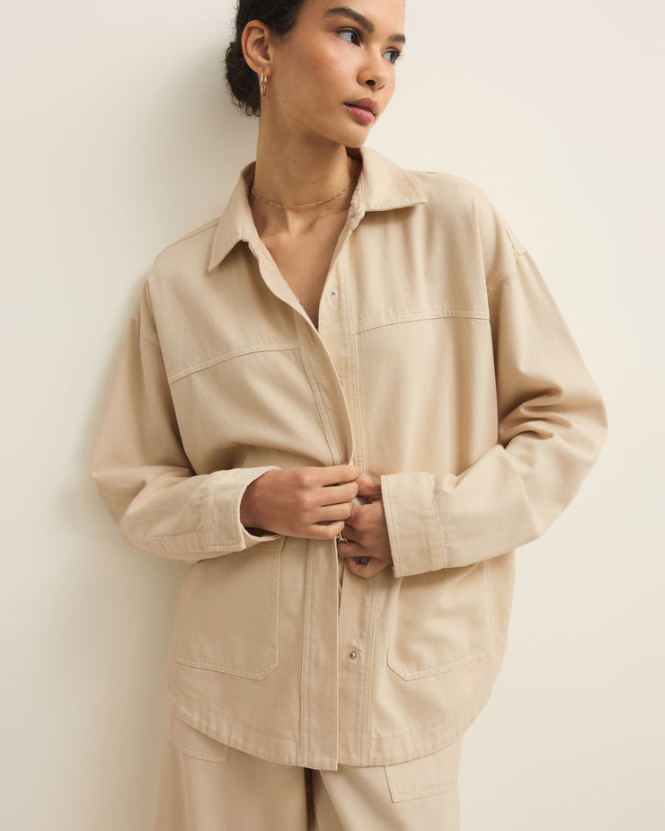 Woman wearing a beige shirt and pants against a plain background