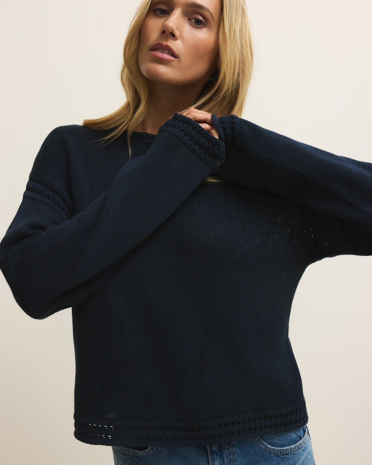 Woman wearing a navy sweater and blue jeans against a plain background