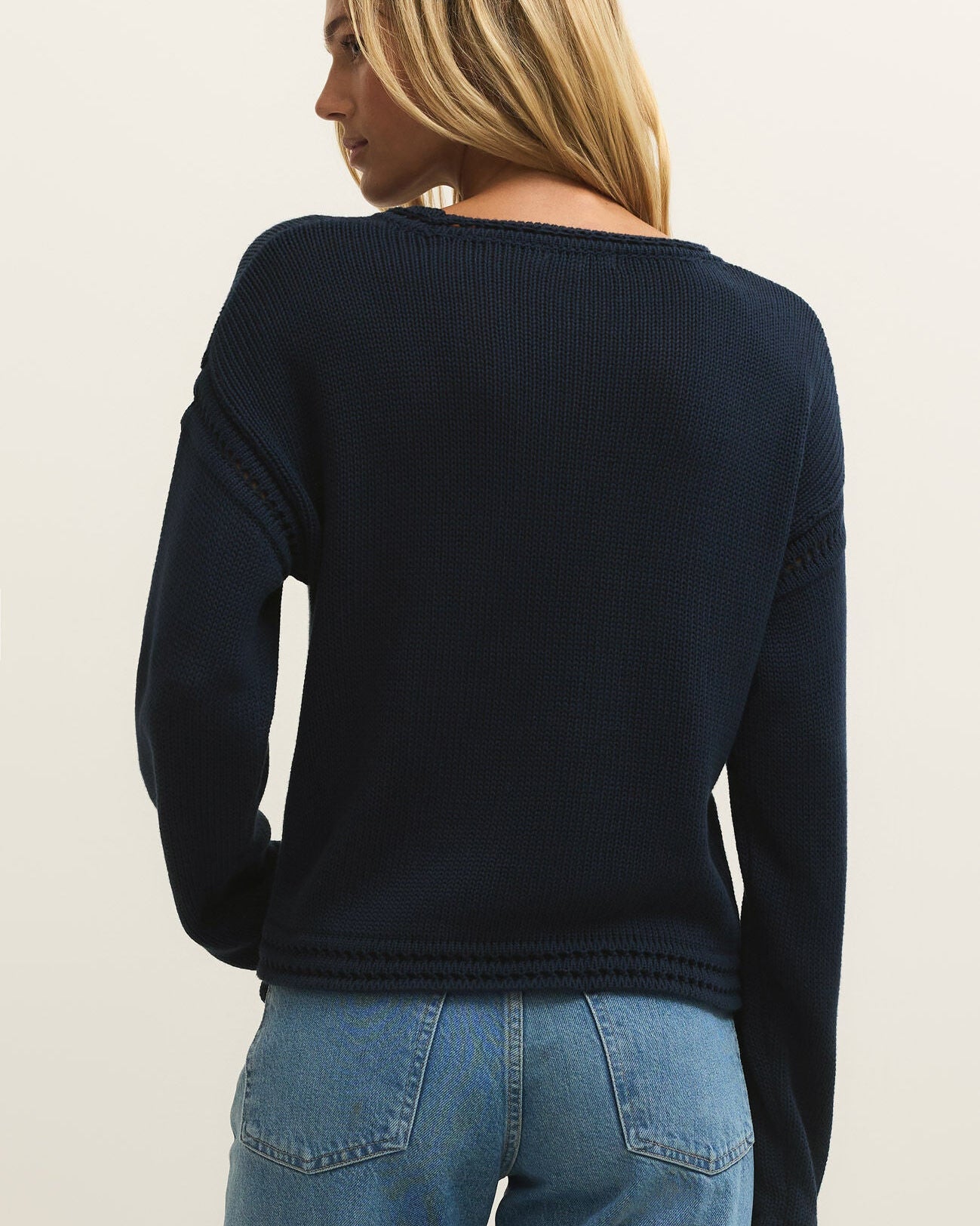 Person wearing a navy sweater and blue jeans on a beige background